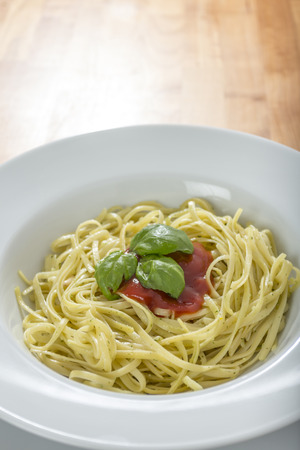 spaghetti witha blot of red sauce and some green basil leaves on wooden tableの写真素材