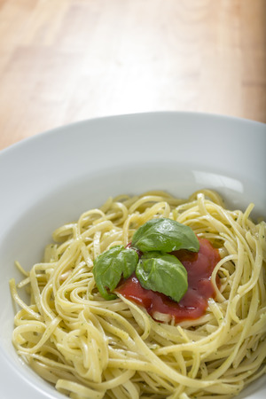 spaghetti witha blot of red sauce and some green basil leaves on wooden tableの写真素材