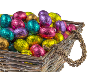 chocolate easter eggs wrapped in colorful aluminum foil in a basket isolated on white backgroundの写真素材