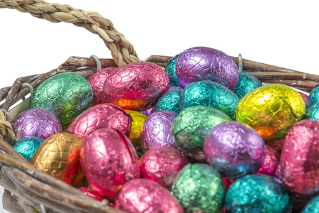 chocolate easter eggs wrapped in colorful aluminum foil in a basket isolated on white background