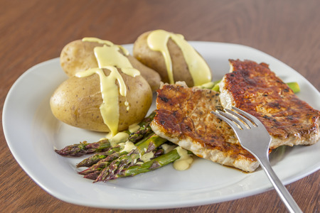 Green Asparagus with potatoes, pork and hollandaise sauce on a white plateの写真素材
