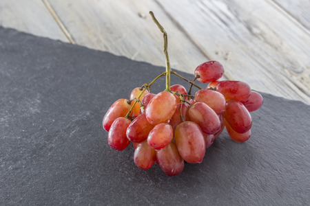 bunch of red grapes on a schist plate on a wooden tableの写真素材