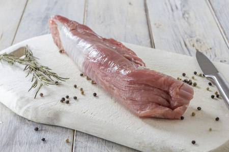 raw fillet of pork on a wooden board with rosemary and pepper in the kitchenの写真素材