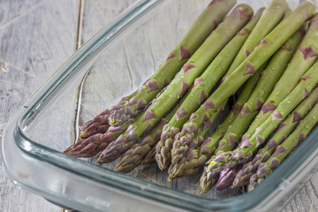 Raw green asparagus in a glass dish on vintage wooden table の写真素材