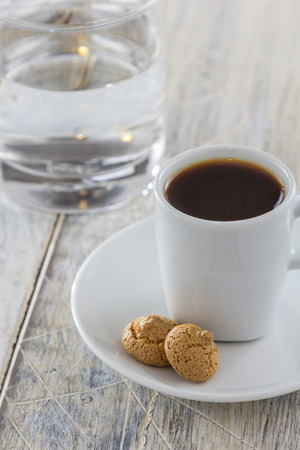 A Cup of espresso with italian amarettini cookies on a wooden table. Traditionally served with a glass of water. の写真素材