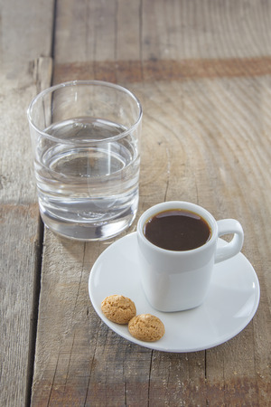 A Cup of espresso with italian amarettini cookies on a wooden table. Traditionally served with a glass of water. の写真素材