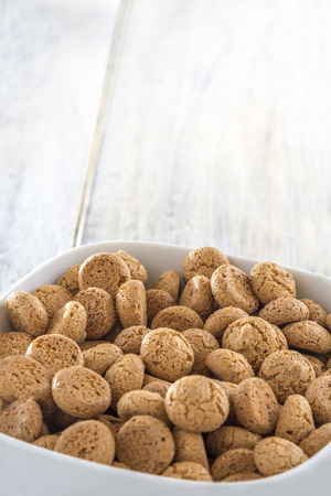 Traditional italian amarettini cookies in a white bowl on a wooden tableの写真素材