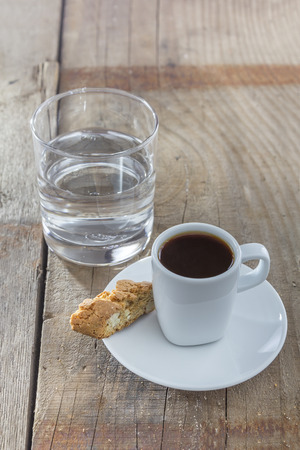 A Cup of espresso with italian biscotti cookies on a wooden table  Traditionally served with a glass of water の写真素材