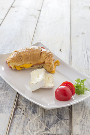 Croisant sandwich with bacon runny cheese and tomatoes and Camembert on a white plateの写真素材