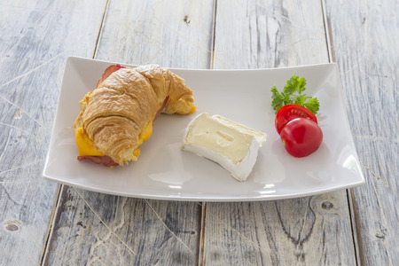 Croisant sandwich with bacon runny cheese and tomatoes and Camembert on a white plateの写真素材