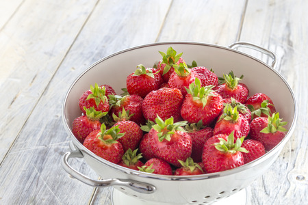Fresh Strawberries in a white enamel sieve on a rustic wooden tableの写真素材