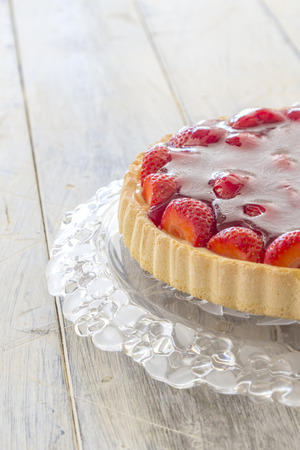 Homemade strawberry cake on a glass platter on a wooden tableの写真素材