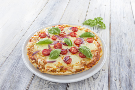 Homemade Pizza with tomatoes red onions and fresh basil on a rustic wooden tableの写真素材