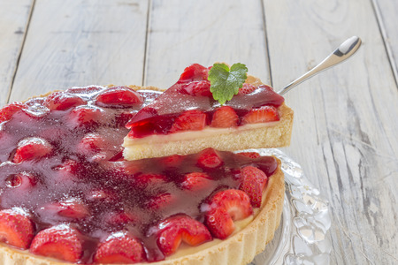 Homemade strawberry cake with one slice lifted up on a glass platter on a wooden tableの写真素材