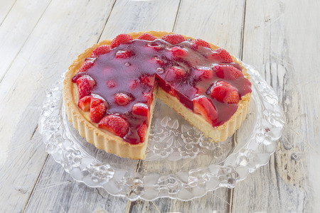Homemade strawberry cake with one slice missing on a glass platter on a wooden tableの写真素材