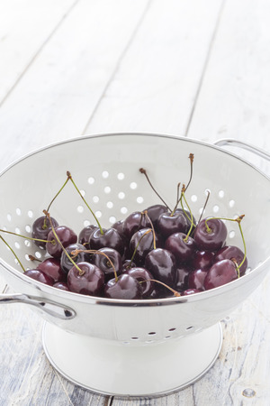 Fresh cherries in a white sieve on a wooden tableの写真素材