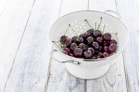 Fresh cherries in a white sieve on a wooden tableの写真素材