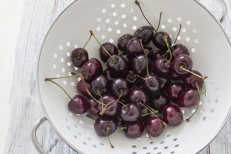 Fresh cherries in a white sieve on a wooden tableの写真素材