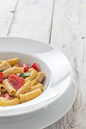 Tortiglioni Pasta with roasted chicken breast and tomatoes on a white plateの写真素材