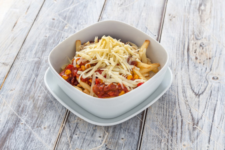french fries with chilli and cheese in a bowl on a rustic white tableの写真素材