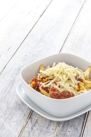 french fries with chilli and cheese in a bowl on a rustic white tableの写真素材