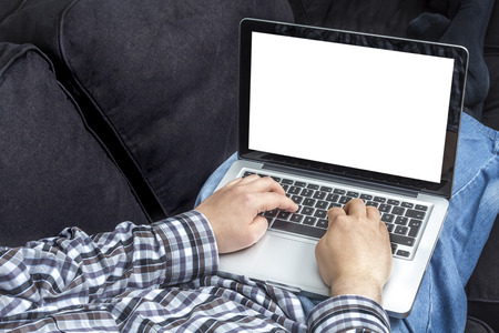 Man in checkered shirt relaxing on a couch surfing on a laptop with white isolated screenの写真素材