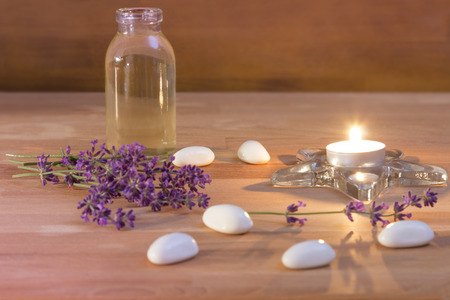 A Tea candle with a bottle of oil white stones and lavender on rustic wooden backgroundの写真素材