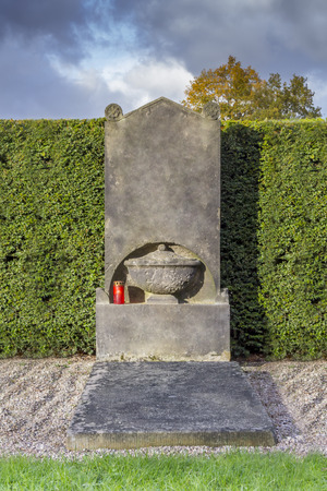 Weathered historic Tombstone with a red candle in front of a green hedgeの写真素材