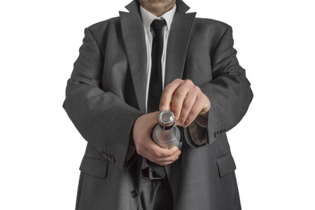 A man in a gray coat opening a bottle of champagne pointing at the camera isolated on white backgroundの写真素材