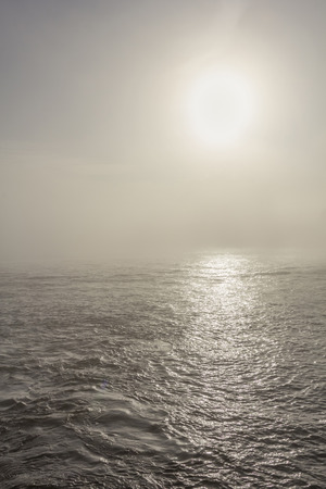 Sun shining through dense fog reflecting on the water.の写真素材