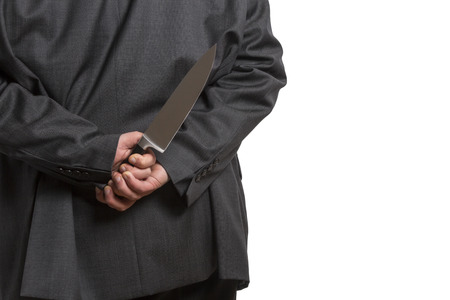 Man in suit hiding a large knife behind his back isolated on white backgroundの写真素材