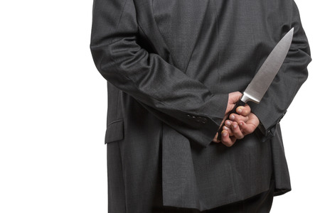 Man in suit hiding a large knife behind his back isolated on white backgroundの写真素材