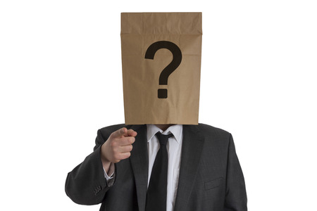 A Man in suit with a paper bag with a question mark on his head pointing into the camera isolated on white backgroundの写真素材