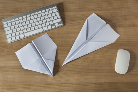 Two Paper Airplanes on a wooden office desk with modern keyboard and mouseの写真素材