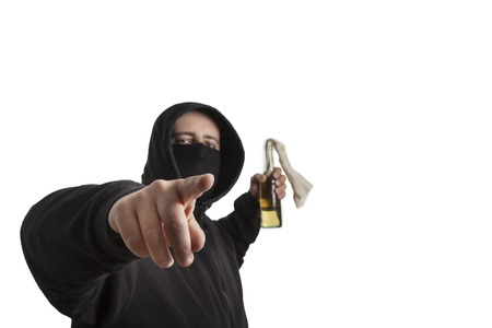 Hooded man in black dress holding a molotov cocktail pointing into the camera isolated on white...