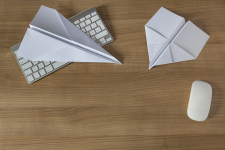 Two Paper Airplanes on a wooden office desk with modern keyboard and mouseの写真素材