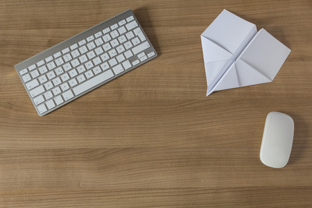 Paper Airplane on a wooden office desk with modern keyboard and mouseの写真素材