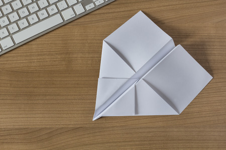 Paper Airplane on a wooden office desk with modern keyboardの写真素材