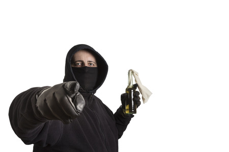 Hooded man in black dress holding a molotov cocktail pointing into the camera isolated on white backgroundの写真素材