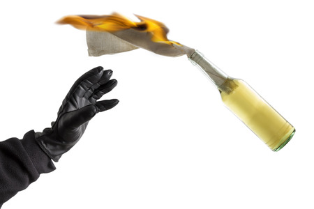 Arm in black sleeve with black leather glove thwowing a Molotov Cocktail with burning fuse, isolated on white backgroundの写真素材