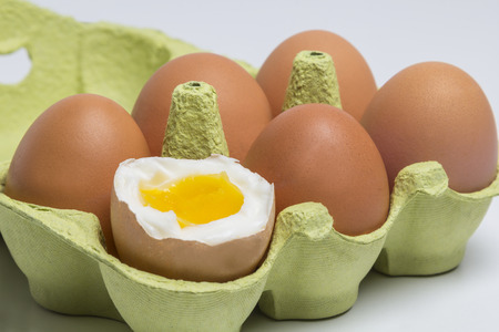 Box of Eggs with one broken boiled egg on white backgroundの写真素材