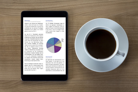A tablet computer with tables and statistics and a cup of coffee on a wooden desktopの写真素材