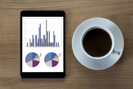 A tablet computer on tables with statistics and a cup of coffee on woodenの写真素材