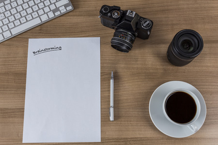A sheet with the word brainstorming, modern keyboard, vintage camera and a cup of coffee on woodenの写真素材