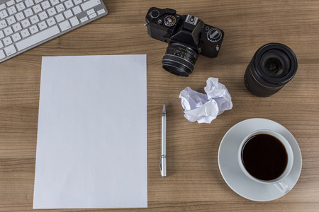 A blank sheet, modern keyboard, vintage camera and a cup of coffee on a wooden desktopの写真素材