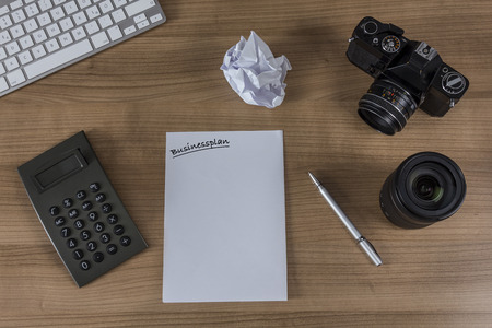 Modern keyboard, calculator, sheet with the word businessplan, vintage camera and a pen on a wooden desktopの写真素材