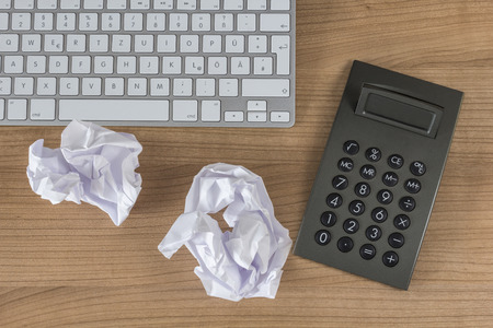 Modern keyboard a calculator and two crumpled paper sheets on a wooden Desktopの写真素材