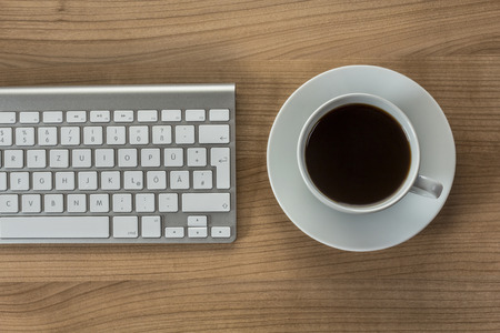Modern keyboard and a cup of coffee on a wooden Desktopの写真素材