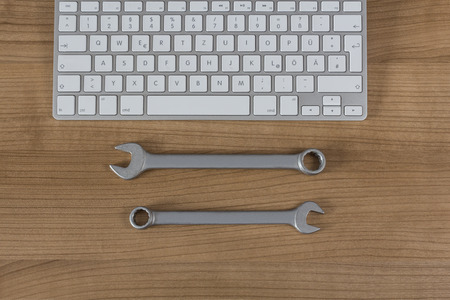 Modern keyboard and two wrenches on a wooden Desktopの写真素材