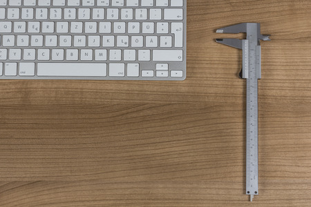 Modern keyboard and a sliding caliper on a wooden Desktopの写真素材